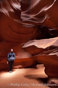 A hiker admiring the striated walls and dramatic light within Antelope Canyon, a deep narrow slot canyon formed by water and wind erosion, Navajo Tribal Lands, Page, Arizona