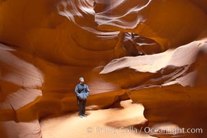 A hiker admiring the striated walls and dramatic light within Antelope Canyon, a deep narrow slot canyon formed by water and wind erosion, Navajo Tribal Lands, Page, Arizona