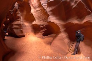A photographer works amidst the striated walls and dramatic light within Antelope Canyon, a deep narrow slot canyon formed by water and wind erosion, Navajo Tribal Lands, Page, Arizona