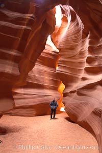 A hiker admiring the striated walls and dramatic light within Antelope Canyon, a deep narrow slot canyon formed by water and wind erosion, Navajo Tribal Lands, Page, Arizona