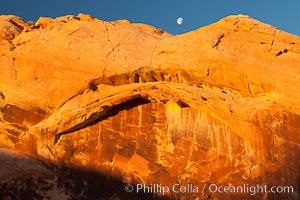 Setting moon over natural sandstone arch, sunrise.