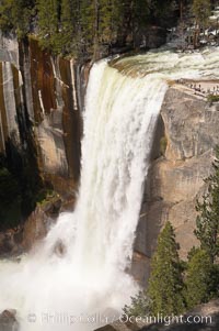 Vernal Falls at peak flow in late spring.  Hikers are visible at the precipice of the waterfall.  Viewed from the John Muir Trail.  Vernal Falls drops 317 through a joint in the narrow Little Yosemite Valley, Yosemite National Park, California