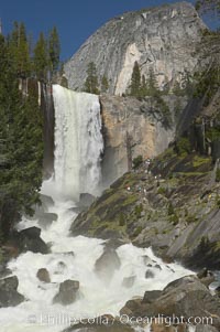 Vernal Falls and the Merced River, at peak flow in late spring.  Hikers ascending the Mist Trail visible at right.  Vernal Falls drops 317 through a joint in the narrow Little Yosemite Valley, Yosemite National Park, California