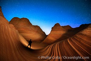 The Wave at Night, under a clear night sky full of stars.  Photographer is illuminating the striated rocks with a small handheld light. The Wave, an area of fantastic eroded sandstone featuring beautiful swirls, wild colors, countless striations, and bizarre shapes set amidst the dramatic surrounding North Coyote Buttes of Arizona and Utah. The sandstone formations of the North Coyote Buttes, including the Wave, date from the Jurassic period. Managed by the Bureau of Land Management, the Wave is located in the Paria Canyon-Vermilion Cliffs Wilderness and is accessible on foot by permit only.