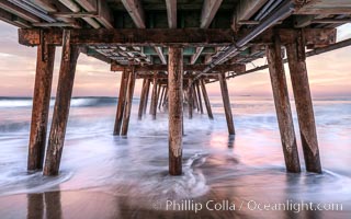 Waves break on the Imperial Beach Pier pilings, at dawn with colorful sunrise clouds over the ocean