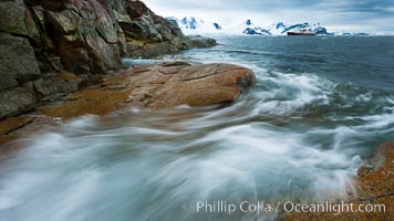 Waves rush in, sunset, Antarctica.  Ocean water rushes ashore over the rocky edge of Peterman Island, Antarctica