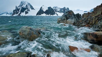 Waves rush in, sunset, Antarctica.  Ocean water rushes ashore over the rocky edge of Peterman Island, Antarctica