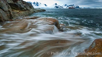 Waves rush in, sunset, Antarctica.  Ocean water rushes ashore over the rocky edge of Peterman Island, Antarctica