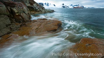 Waves rush in, sunset, Antarctica.  Ocean water rushes ashore over the rocky edge of Peterman Island, Antarctica