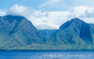 West Maui mountains rise above the coast of Maui, with clouds flanking the ancient eroded remnants of a volcano
