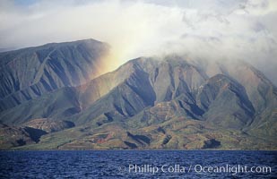 West Maui mountains rise above the coast of Maui, with clouds flanking the ancient eroded remnants of a volcano.