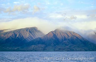 West Maui mountains rise above the coast of Maui, with clouds flanking the ancient eroded remnants of a volcano