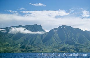 West Maui mountains rise above the coast of Maui, with clouds flanking the ancient eroded remnants of a volcano