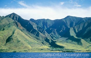 West Maui mountains rise above the coast of Maui, with clouds flanking the ancient eroded remnants of a volcano.