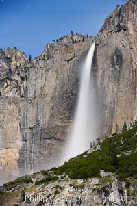 Upper Yosemite Falls by moonlight, viewed from Cooks Meadow. Star trails appear in the night sky. Yosemite Valley, Yosemite National Park, California