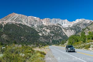 A car passes below stunning High Sierra peaks and mountains as it travels eastward on the Tioga Pass road from Yosemite to the town of Lee Vining. California, Yosemite National Park