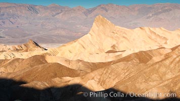 Zabriskie Point, sunrise.  Manly Beacon rises in the center of an eroded, curiously banded area of sedimentary rock, with the Panamint Mountains visible in the distance, Death Valley National Park, California