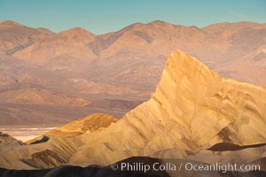 Zabriskie Point, sunrise.  Manly Beacon rises in the center of an eroded, curiously banded area of sedimentary rock, with the Panamint Mountains visible in the distance, Death Valley National Park, California