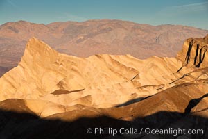 Zabriskie Point, sunrise.  Manly Beacon rises in the center of an eroded, curiously banded area of sedimentary rock, with the Panamint Mountains visible in the distance, Death Valley National Park, California