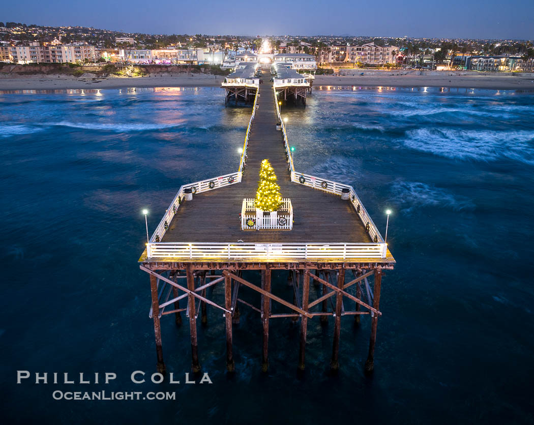 Aerial photo of Crystal Pier with Holiday Christmas Lights at night. The Crystal Pier, Holiday Lights and Pacific Ocean at sunset, waves blur as they crash upon the sand. Crystal Pier, 872 feet long and built in 1925, extends out into the Pacific Ocean from the town of Pacific Beach. California, USA, natural history stock photograph, photo id 40000