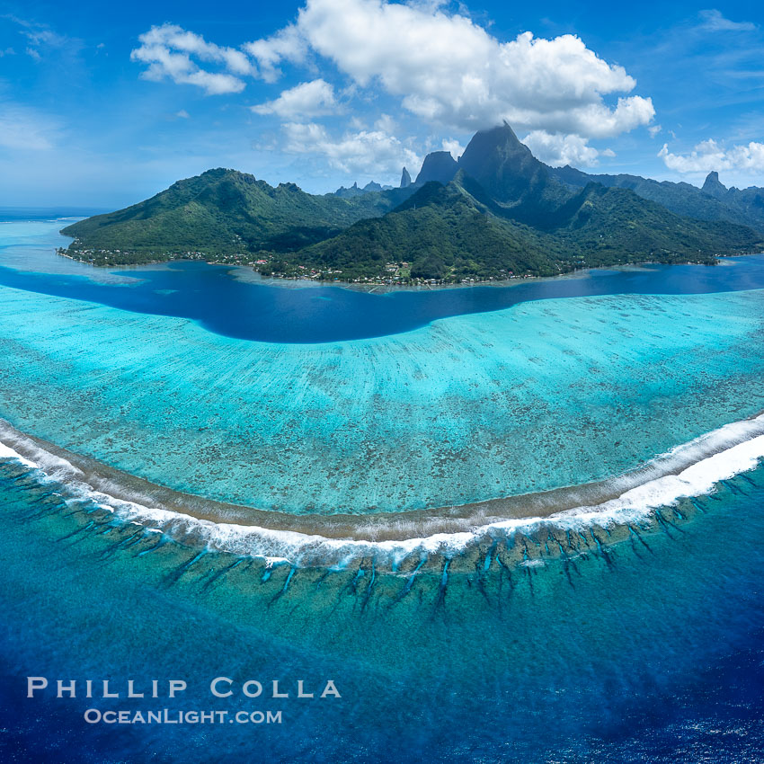Aerial Panorama of the Barrier Reef around Moorea Island, French Polynesia. The outer reef slope is seen adjacent to deep blue oceanic water with white waves breaking against the reef edge. Next, a wide shallow reef flat occurs dotted with coral bommies. Inside of that, a shallow protected lagoon is formed against the island. Tall, rugged, eroded mountains are seen hinting at the age of the ancient volcano that originally formed the island and that is now sinking back down, leaving the encircling reef behind., natural history stock photograph, photo id 41407