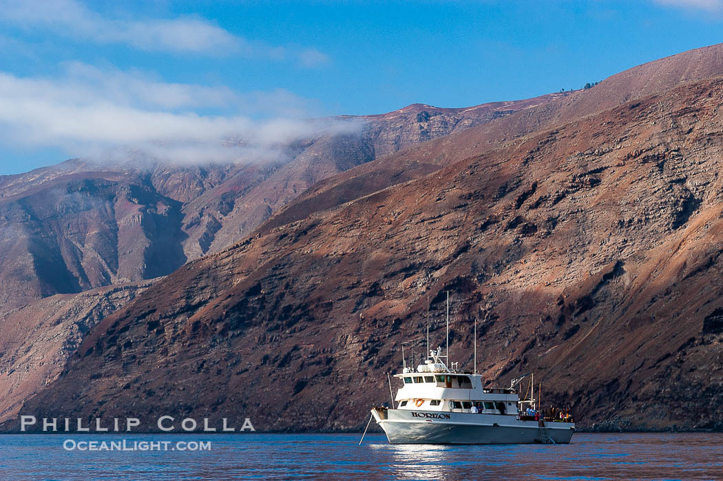 Guadalupe Islands mountainous terrain and sea cliffs tower above the dive boat Horizon while at anchor in Spanish Cove, near the north end of Guadalupe Island (Isla Guadalupe)., natural history stock photograph, photo id 09737