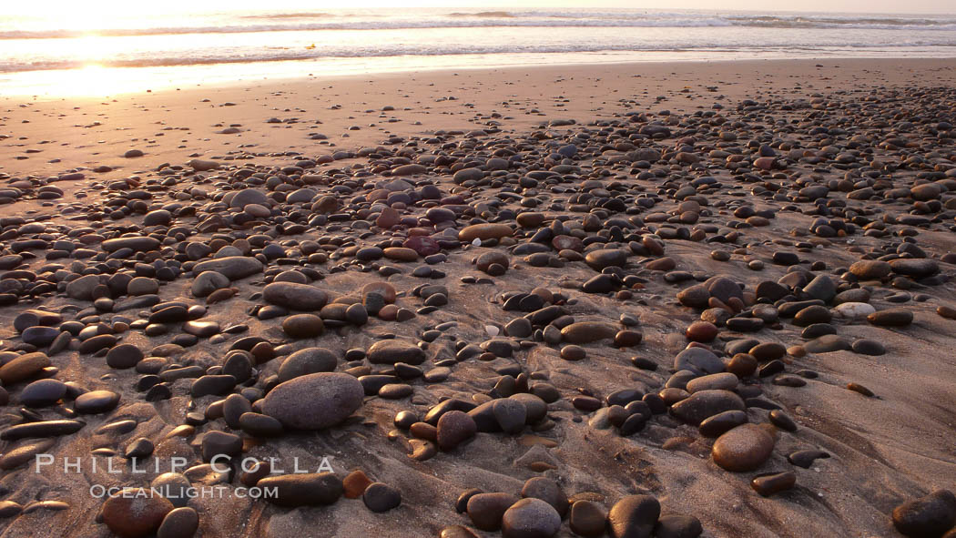 Cobblestones on a flat sand beach.  Cobble stones are polished round and smooth by years of wave energy.  They are alternately exposed and covered by sand depending on the tides, waves and seasons of the year.  Cobblestones are common on the beaches of southern California, contained in the sandstone bluffs along the beach and released onto the beach as the bluffs erode. Carlsbad, USA, natural history stock photograph, photo id 19818