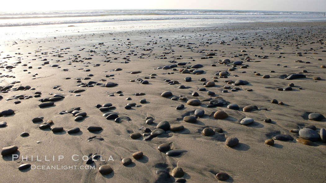 Cobblestones on a flat sand beach.  Cobble stones are polished round and smooth by years of wave energy.  They are alternately exposed and covered by sand depending on the tides, waves and seasons of the year.  Cobblestones are common on the beaches of southern California, contained in the sandstone bluffs along the beach and released onto the beach as the bluffs erode. Carlsbad, USA, natural history stock photograph, photo id 19830