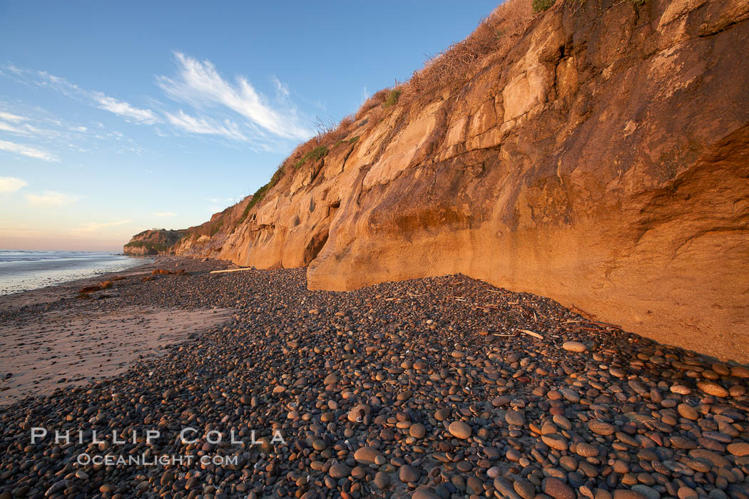Cobblestones piled at the base of seacliffs, sunset.  Beach cliffs made of soft clay continually erode, adding fresh sand and cobble stones to the beach.  The sand will flow away with ocean currents, leading for further erosion of the cliffs. Carlsbad, California, USA, natural history stock photograph, photo id 22190