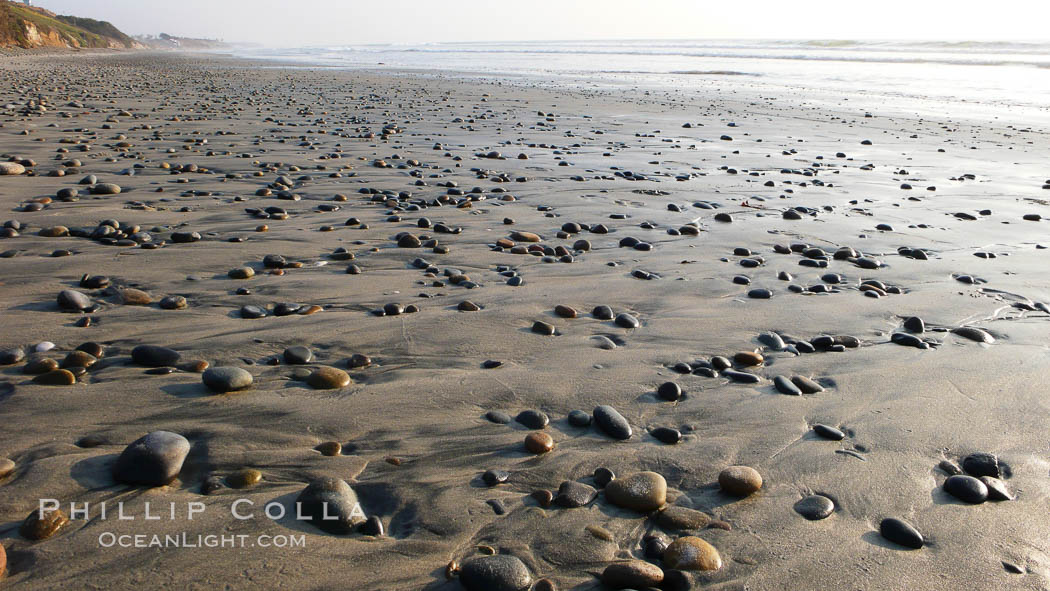 Cobblestones on a flat sand beach.  Cobble stones are polished round and smooth by years of wave energy.  They are alternately exposed and covered by sand depending on the tides, waves and seasons of the year.  Cobblestones are common on the beaches of southern California, contained in the sandstone bluffs along the beach and released onto the beach as the bluffs erode. Carlsbad, USA, natural history stock photograph, photo id 19825