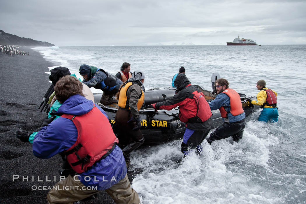 Cheesemans Ecology Safaris tour leaders, work in the surf on a steep black sand beach at Bailey Head to assist tourists land ashore and handle the landing craft: an inflatable zodiac.  The icebreaker M/V Polar Star is anchored in the distance. Deception Island, Antarctic Peninsula, Antarctica, natural history stock photograph, photo id 25458