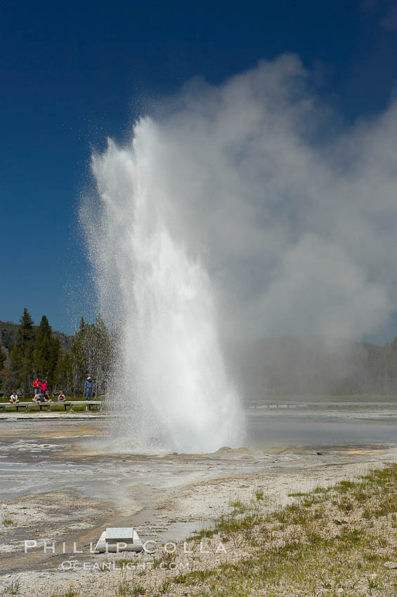 Daisy Geyser erupting with visitors visible in the distance..  Daisy Geyser, a cone-type geyser that shoots out of the ground diagonally, is predictable with intervals ranging from 120 to over 200 minutes.  It reaches heights of 75 feet, lasts 3 to 4 minutes and rarely erupts in concert with nearby Splendid Geyser.  Upper Geyser Basin. Yellowstone National Park, Wyoming, USA, natural history stock photograph, photo id 13384