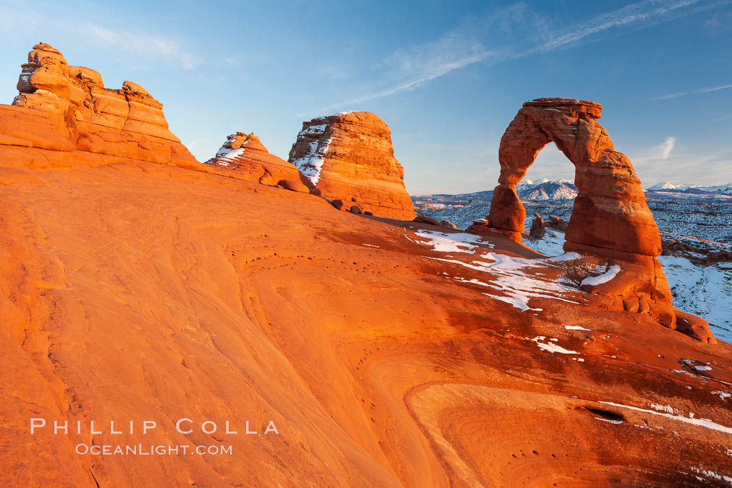Delicate Arch, dusted with snow, at sunset, with the snow-covered La Sal mountains in the distance.  Delicate Arch stands 45 feet high, with a span of 33 feet, atop of bowl of slickrock sandstone. Arches National Park, Utah, USA, natural history stock photograph, photo id 18109