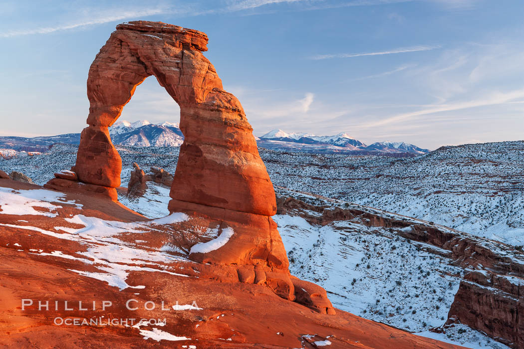 Delicate Arch, dusted with snow, at sunset, with the snow-covered La Sal mountains in the distance.  Delicate Arch stands 45 feet high, with a span of 33 feet, atop of bowl of slickrock sandstone. Arches National Park, Utah, USA, natural history stock photograph, photo id 18113