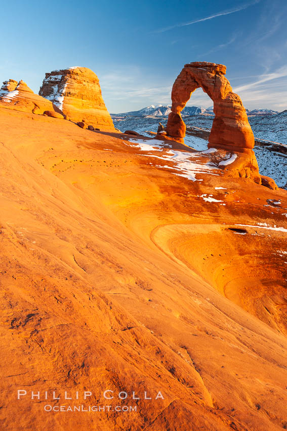 Delicate Arch, dusted with snow, at sunset, with the snow-covered La Sal mountains in the distance.  Delicate Arch stands 45 feet high, with a span of 33 feet, atop of bowl of slickrock sandstone. Arches National Park, Utah, USA, natural history stock photograph, photo id 18106