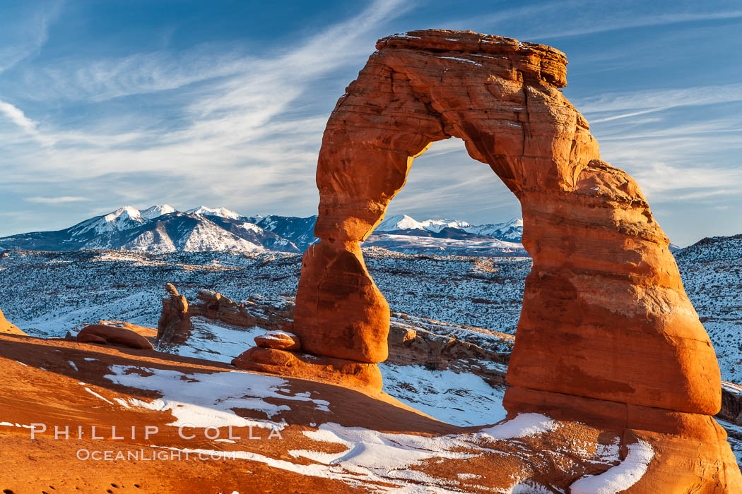 Delicate Arch, dusted with snow, at sunset, with the snow-covered La Sal mountains in the distance.  Delicate Arch stands 45 feet high, with a span of 33 feet, atop of bowl of slickrock sandstone. Arches National Park, Utah, USA, natural history stock photograph, photo id 18104