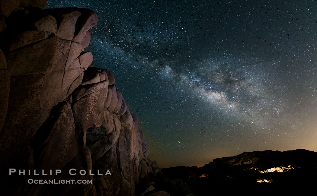 The Milky Way rises above a huge wall of stone, stars fill the night sky and soar over the distant lights of campers., natural history stock photograph, photo id 27899
