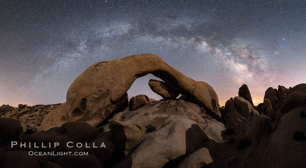 Milky Way during Full Lunar Eclipse over Arch Rock, Joshua Tree National Park, April 4 2015.  The arch and surrounding landscape are illuminated by the faint light of the fully-eclipsed blood red moon.  Light from the sun has passed obliquely through the Earth's thin atmosphere, taking on a red color, and is then reflected off the moon and reaches the Earth again to light the arch.  The intensity of this light is so faint that the Milky Way can be seen clearly at the same time. California, USA, natural history stock photograph, photo id 30717