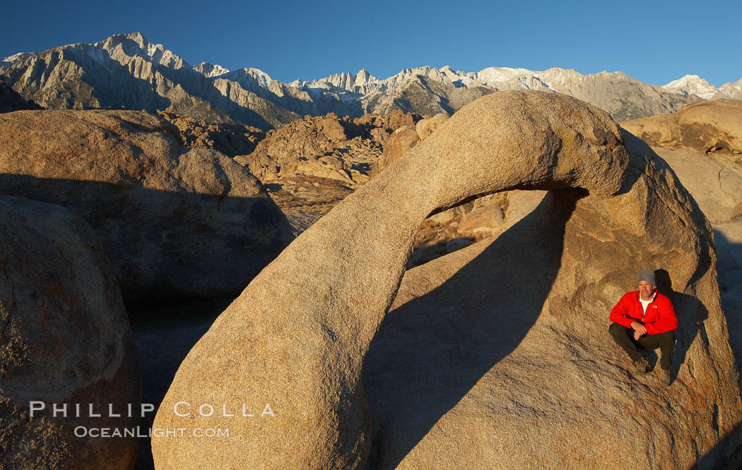 A hiker admires Mobius Arch in early morning golden sunlight, with the snow-covered Sierra Nevada Range and the Alabama Hills seen in the background. Alabama Hills Recreational Area, California, USA, natural history stock photograph, photo id 21769