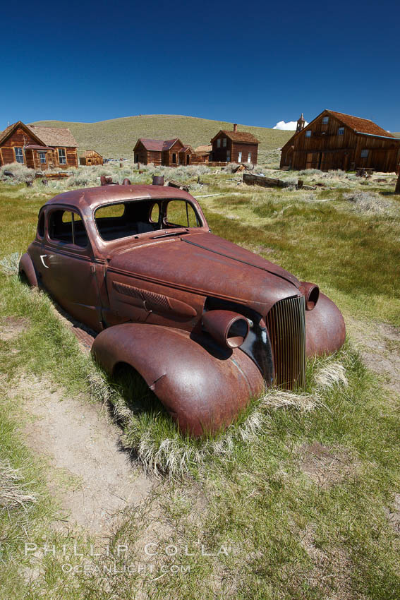 Old car lying in dirt field, Fuller Street and Green Street buildings in background. Bodie State Historical Park, California, USA, natural history stock photograph, photo id 23162