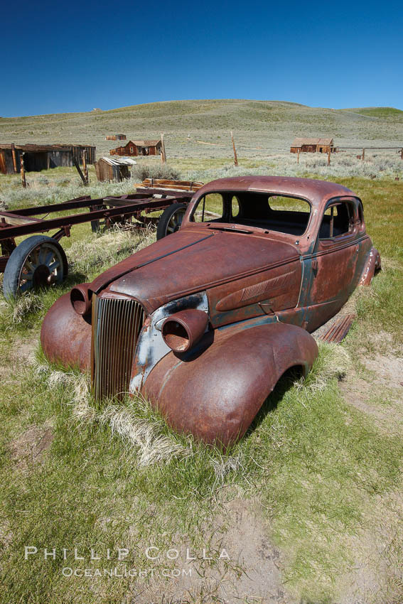 Old car lying in dirt field, Fuller Street and Green Street buildings in background. Bodie State Historical Park, California, USA, natural history stock photograph, photo id 23172