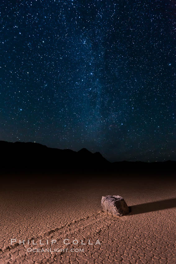 Racetrack sailing stone and Milky Way, at night. A sliding rock of the Racetrack Playa. The sliding rocks, or sailing stones, move across the mud flats of the Racetrack Playa, leaving trails behind in the mud. The explanation for their movement is not known with certainty, but many believe wind pushes the rocks over wet and perhaps icy mud in winter. Death Valley National Park, California, USA, natural history stock photograph, photo id 27638