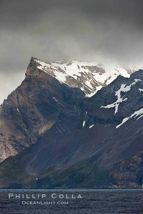 South Georgia Island coastline, showing the island's characteristic rugged topography.  56% of the island is covered by 161 glaciers, which have created numerous large bays and inlets that provide excellent habitat for marine animals and seabirds. Mountains meet the sea in steep-sided seacliffs covered with sparse vegetation.  The highest point on South Georgia Island is Mt. Paget at 2,915m., natural history stock photograph, photo id 24343