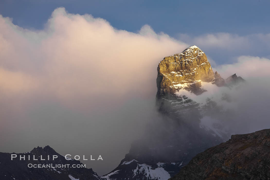 South Georgia Island, spire and sunset clouds, showing the island's characteristic rugged topography.  56% of the island is covered by 161 glaciers, which have created numerous large bays and inlets that provide excellent habitat for marine animals and seabirds. Mountains meet the sea in steep-sided seacliffs covered with sparse vegetation.  The highest point on South Georgia Island is Mt. Paget at 2,915m. Right Whale Bay, natural history stock photograph, photo id 24328