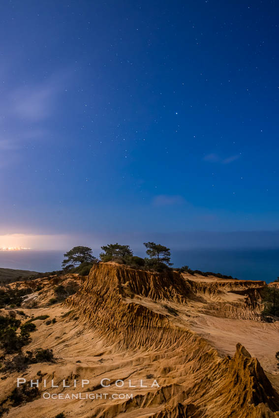 Image 28403, Torrey Pines State Reserve at Night, stars and clouds fill the night sky with the lights of La Jolla visible in the distance. San Diego, California, USA, Phillip Colla, all rights reserved worldwide. Keywords: astrophotography, astrophotography landscape, bluff, broken hill, california, cliff, clouds, coast, eroded, erosion, evening, hill, landscape, landscape astrophotography, nature, night, nightscape, outdoors, outside, park, reserve, san diego, sandstone, scene, scenic, seashore, shore, stars, state parks, storm cloud, torrey pines, torrey pines state park, torrey pines state reserve, usa.